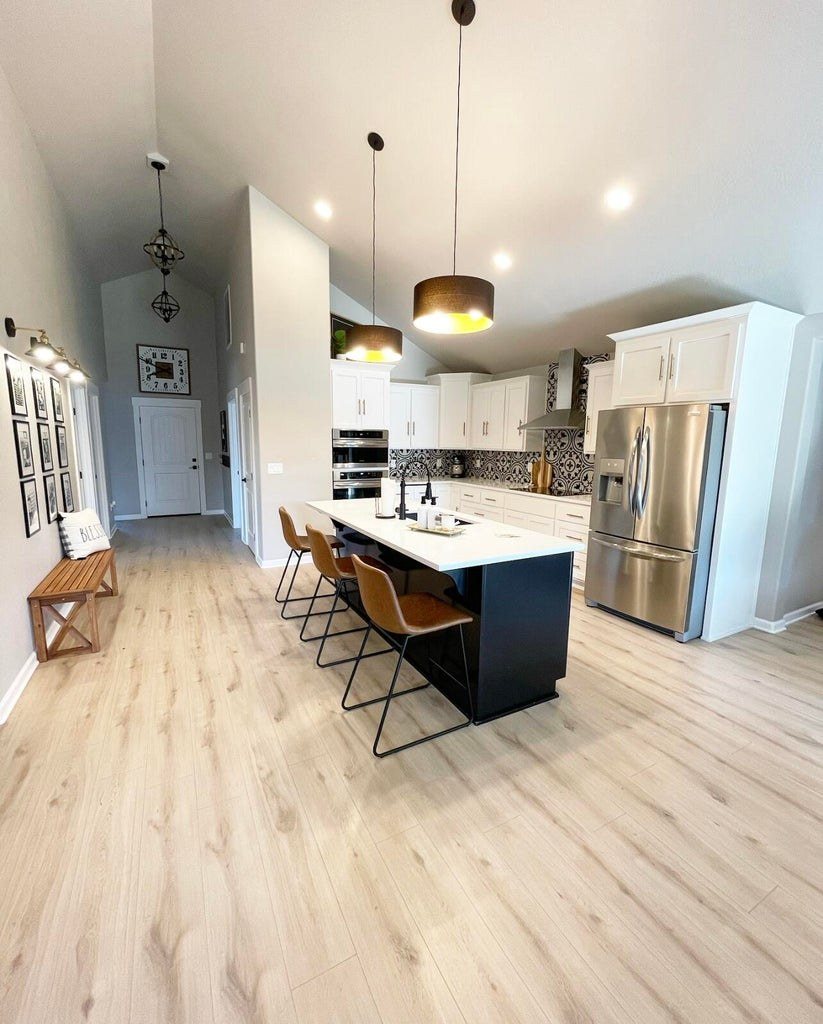 White shaker kitchen with a black quartz island, bar seating and patterned tile backsplash, open to the living space