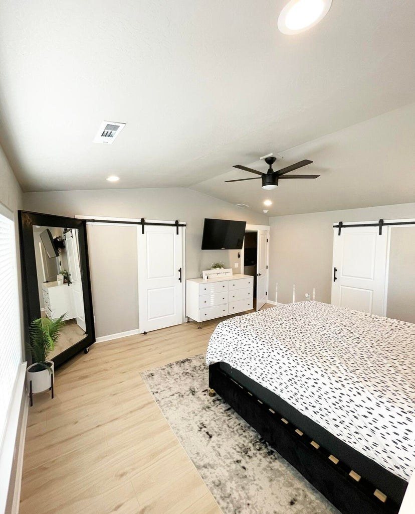 Primary bedroom with a sliding barn door, vaulted ceiling and wide-plank floors